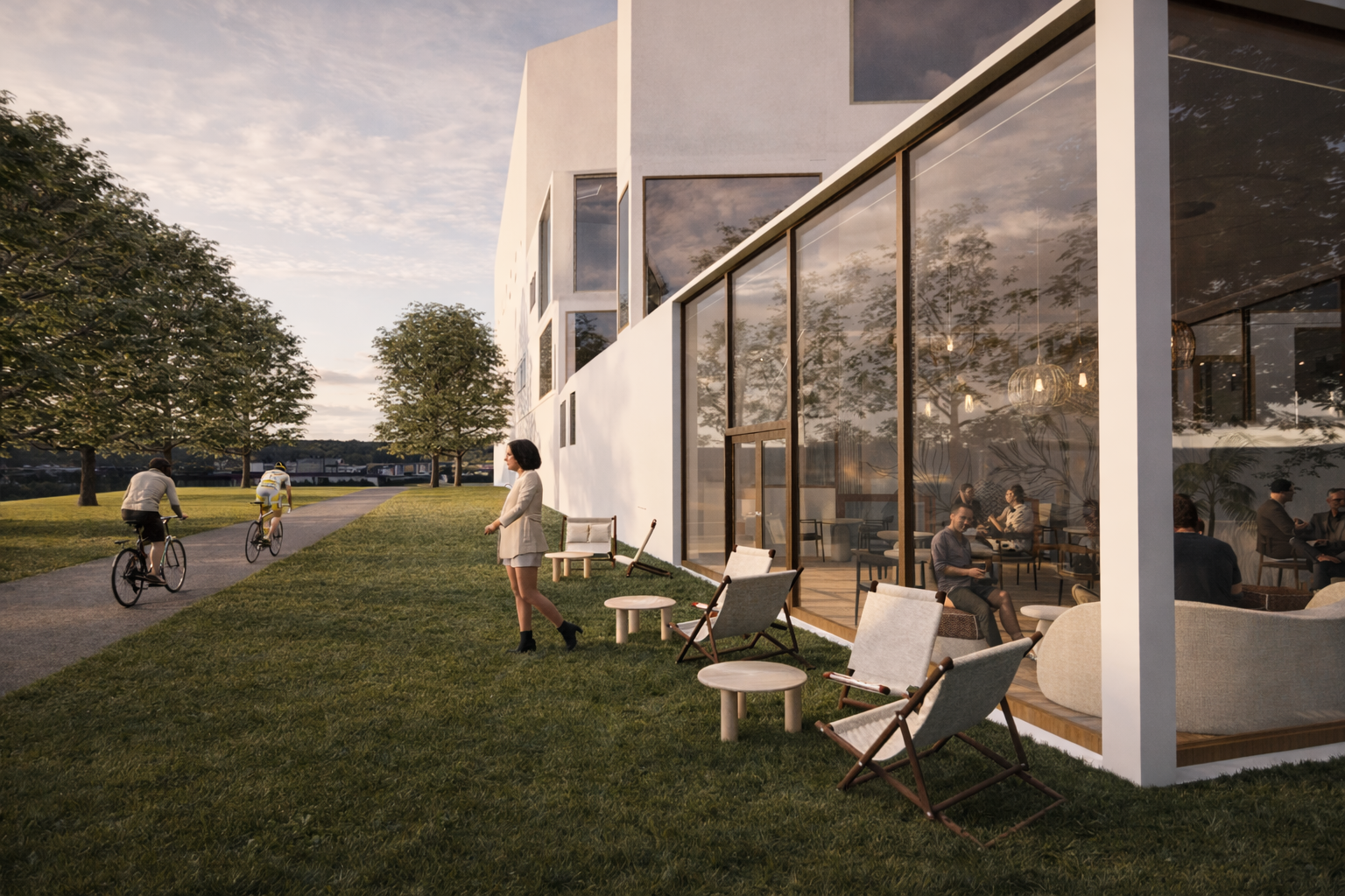 Vue extérieure du bâtiment blanc contemporain au coucher du soleil, grandes baies vitrées, terrasse en bois avec chilongues et allée bordée d’arbres où passent des cyclistes